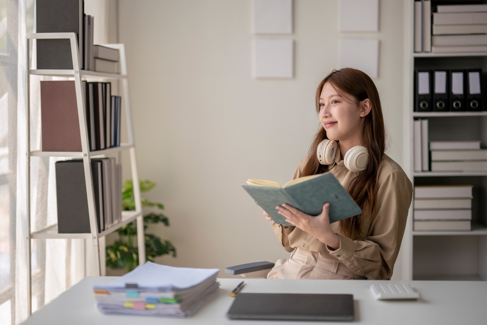 A,Woman,Is,Sitting,At,A,Desk,With,A,Book